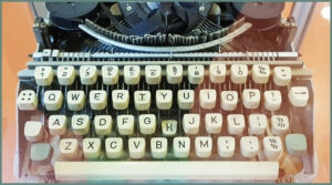Close-up of a typewriter, quite old and battered, behind perspex